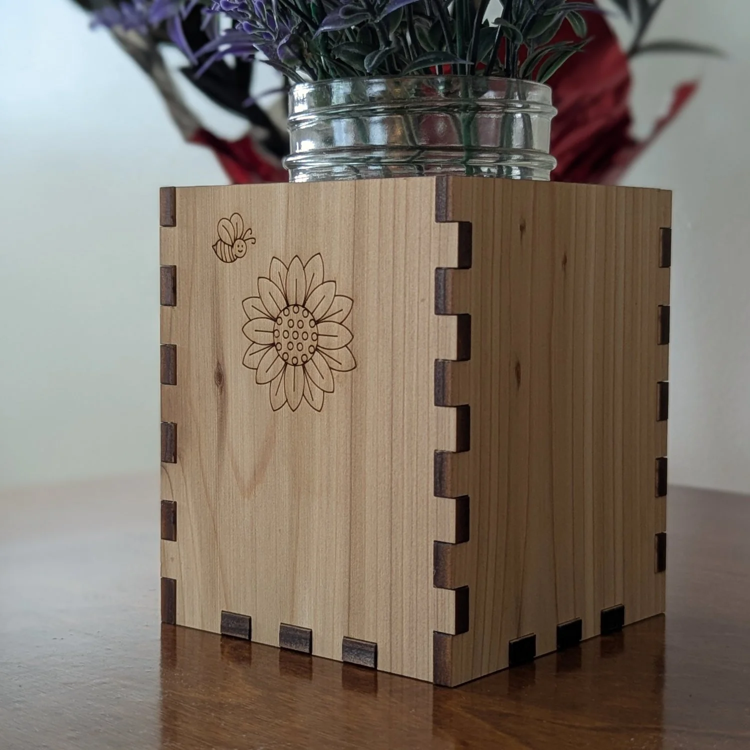 Angled close-up of the vase sleeve highlighting the engraved sunflower and bee design with visible finger-joint construction.