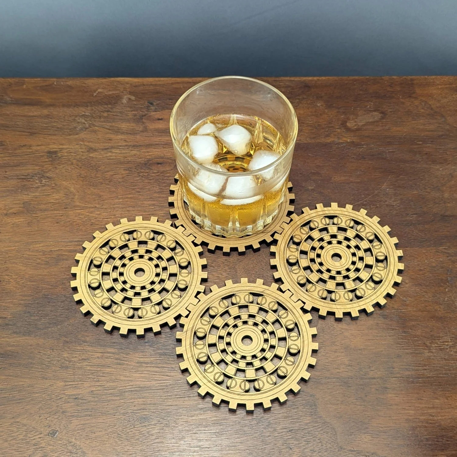Set of four Operator wooden gear coasters with circular dial-like design, glass of whiskey placed on one.