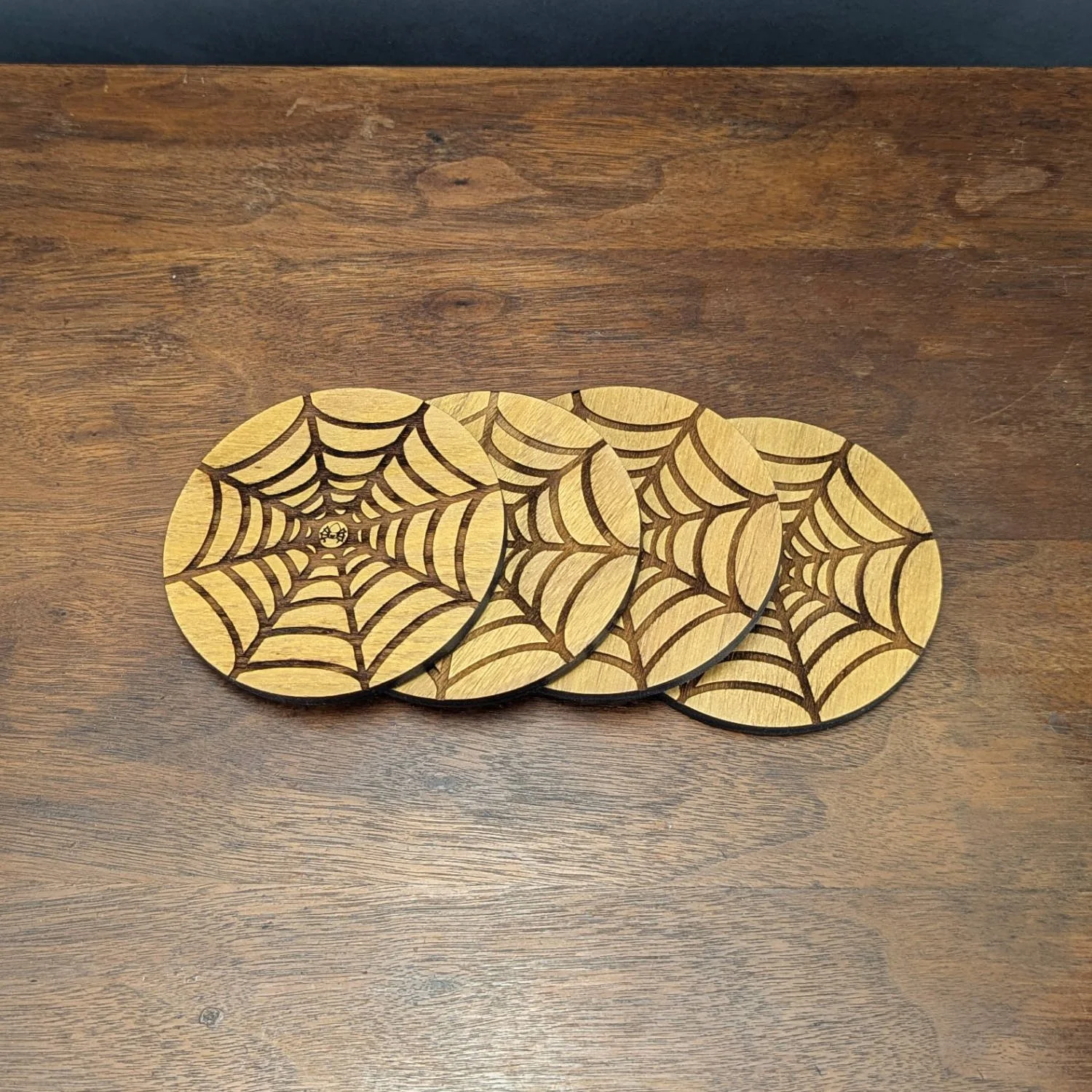 Set of four Shadow Web Coasters arranged in a row on wooden surface