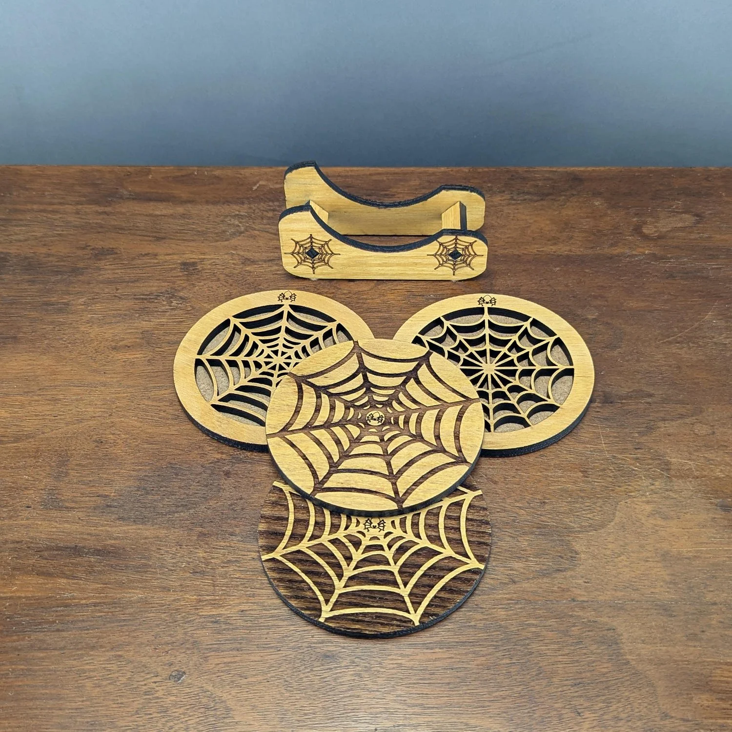 Top view of four unique spiderweb wooden coasters with engraved holder, part of the Webworks Collection Set One.