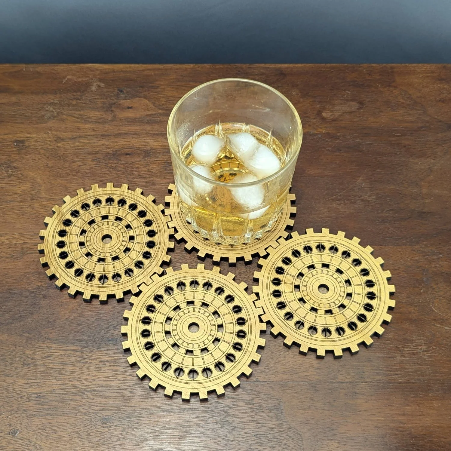 A whiskey glass resting on one gear coaster, with three additional coasters arranged around it.