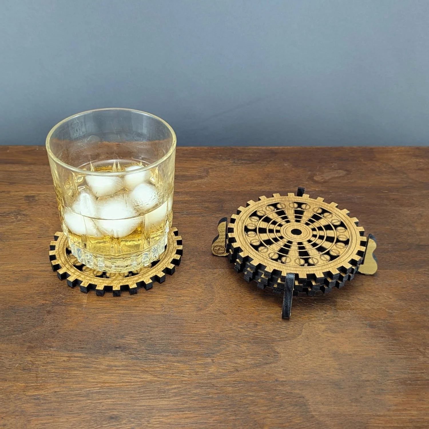 Wooden gear coasters stacked in a stand with glass of whiskey on coaster in front.