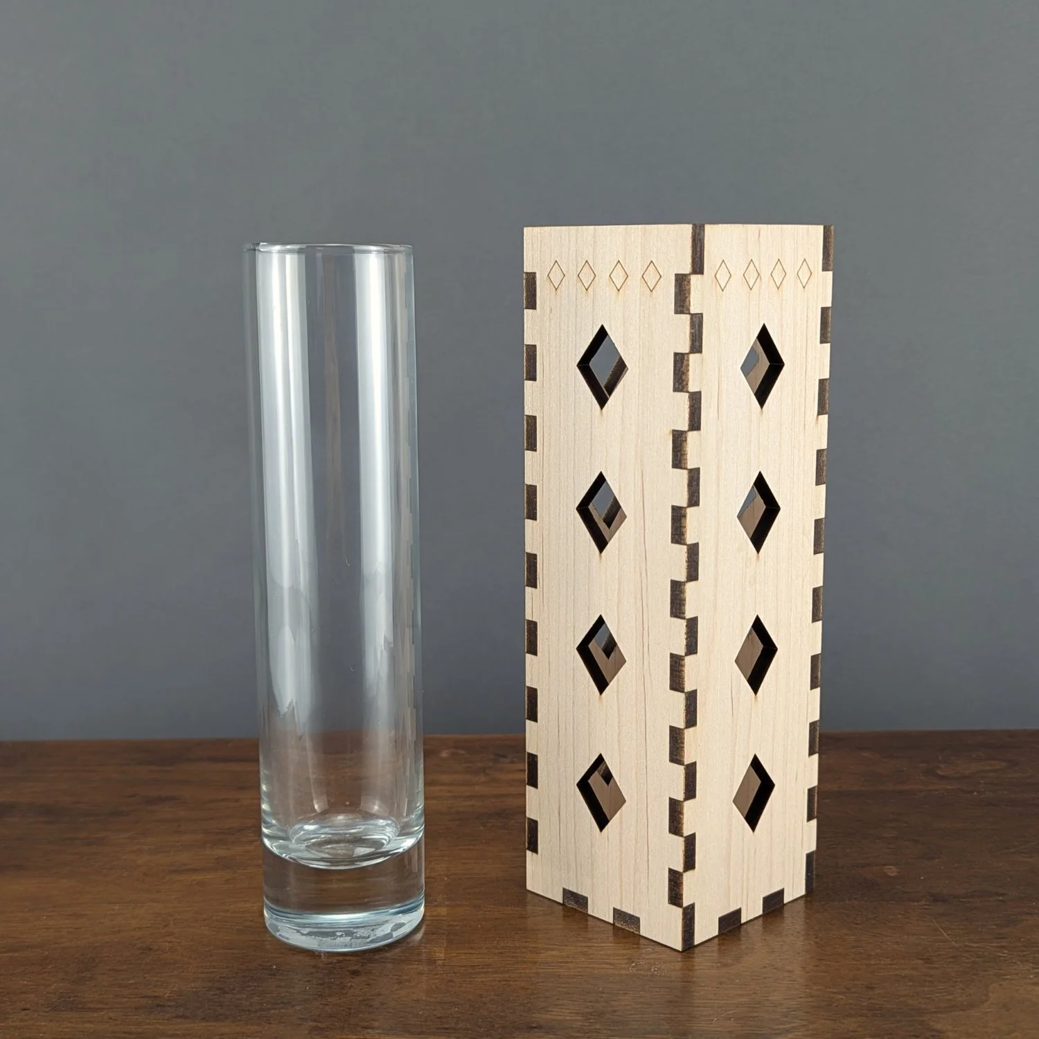 Maple wooden vase sleeve with diamond cutouts shown next to removable clear glass cylinder, side angle.
