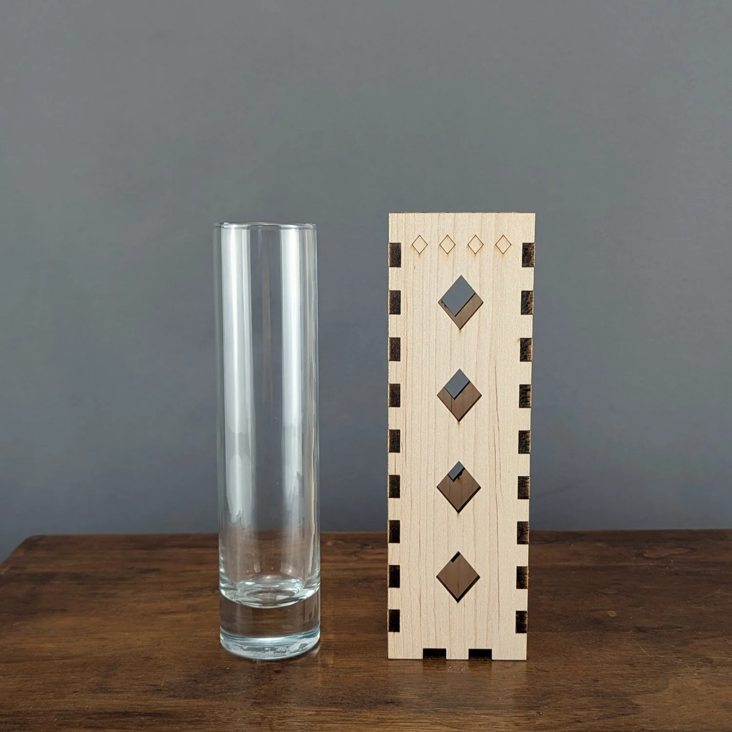 Front view of maple vase sleeve with diamond cutouts alongside its matching glass insert, on a wooden table.