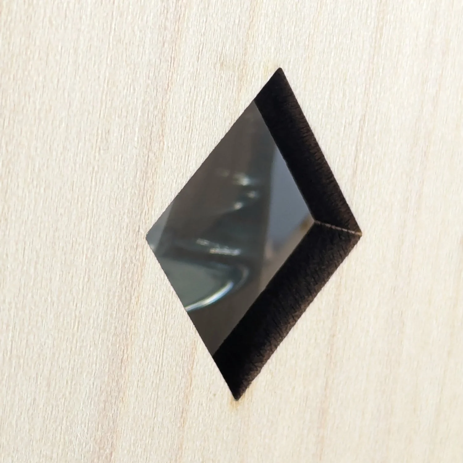 Close-up of diamond-shaped cutout on maple wooden vase sleeve, highlighting smooth laser-cut edges and glass insert behind.