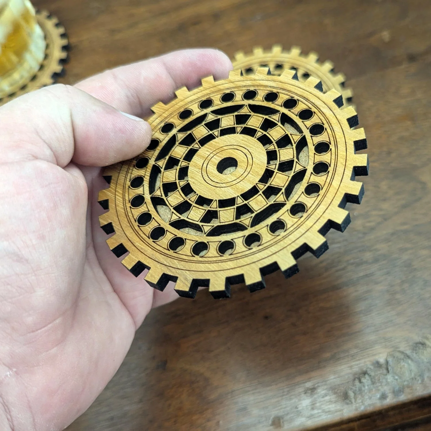 Hand holding The Engineer wooden gear coaster to show size and intricate gear-inspired design.