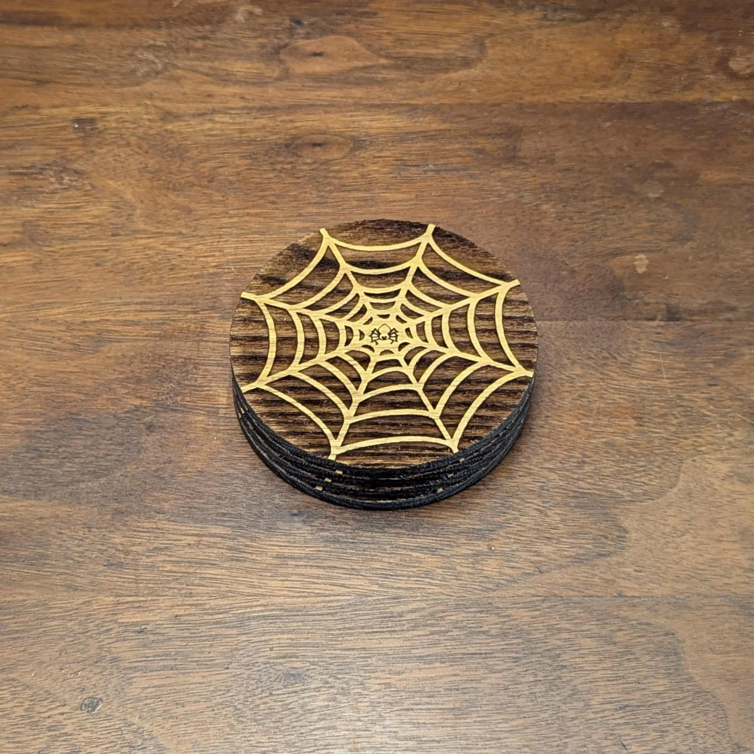 Stack of spiderweb-pattern wooden coasters showing the golden web detail on the top piece.