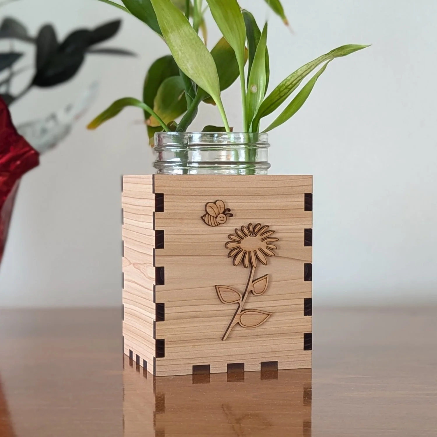 Handcrafted wooden vase box with bee and flower accents, holding a mason jar planter on a polished wooden table.
