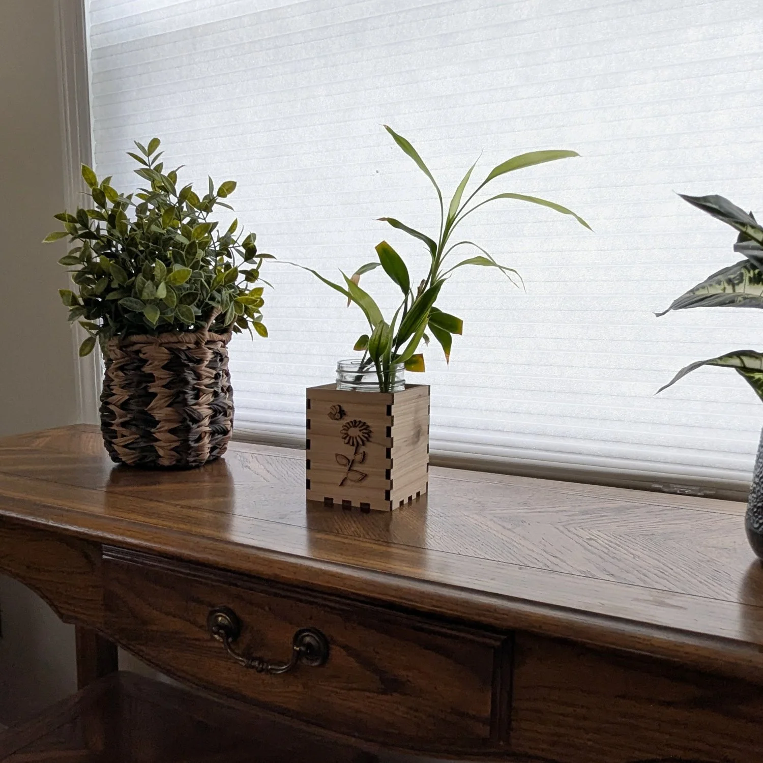 Wooden vase box with mason jar and plant displayed on a console table between decorative potted plants.