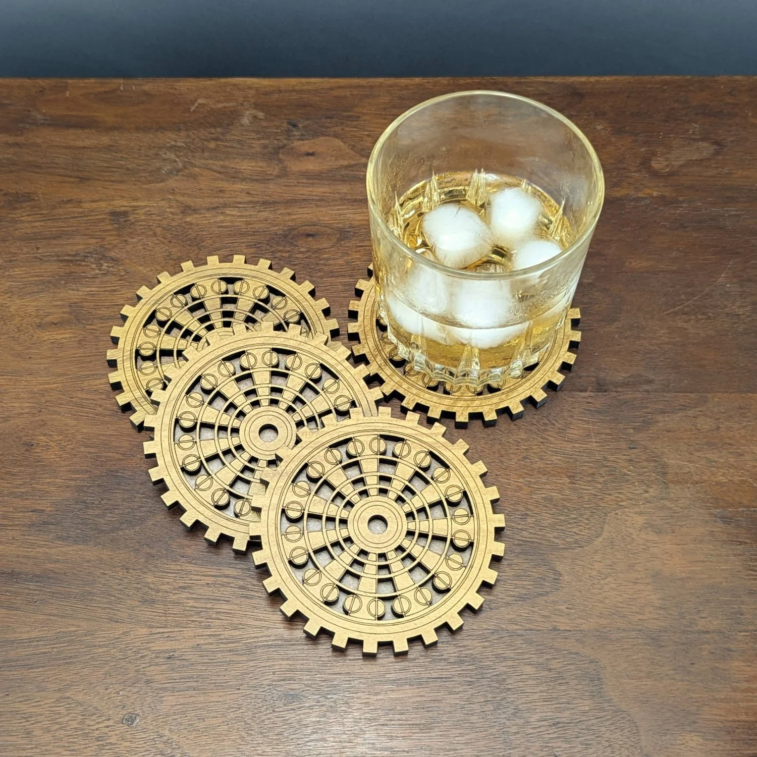 Set of four wooden gear-pattern coasters with a glass of whiskey placed on one.