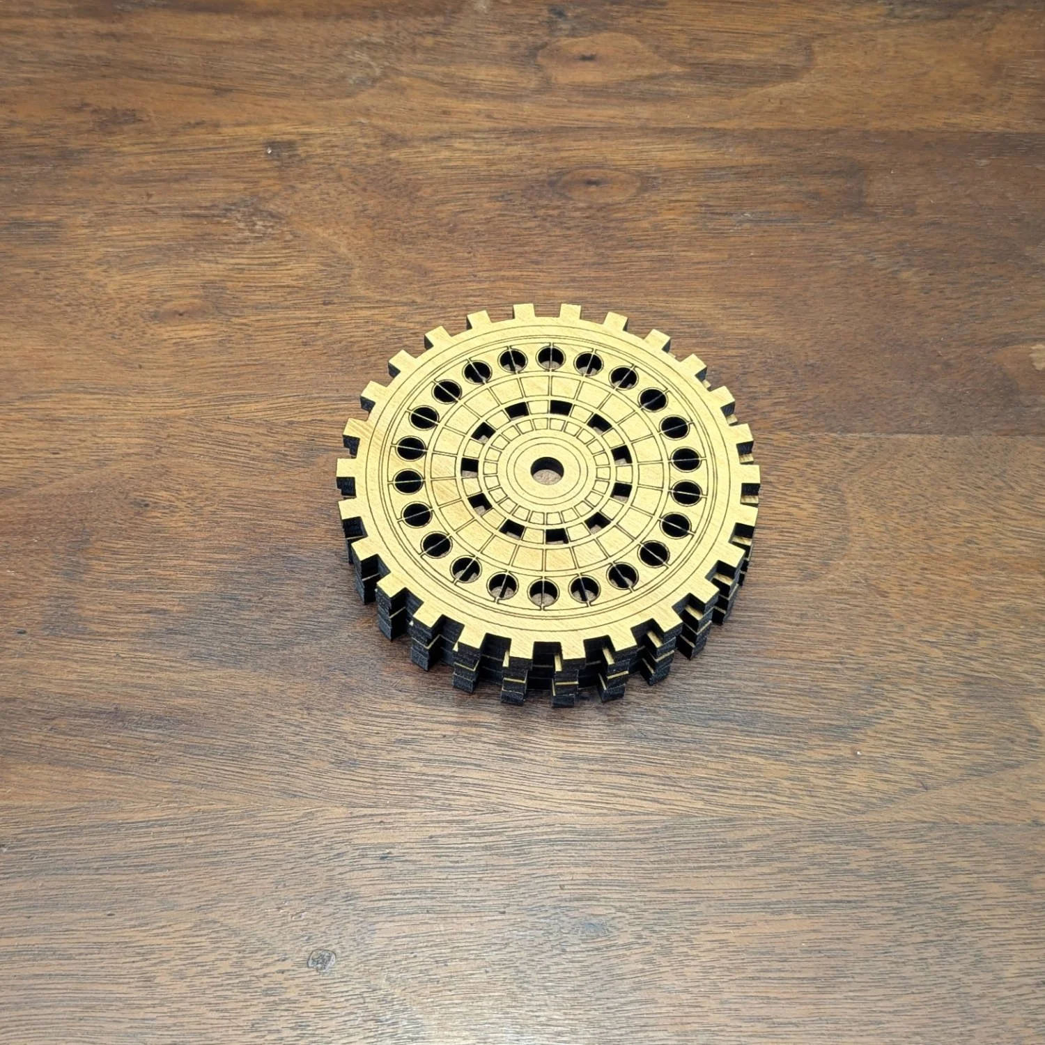 Stack of round wooden gear coasters with intricate cutout design on a wood table.