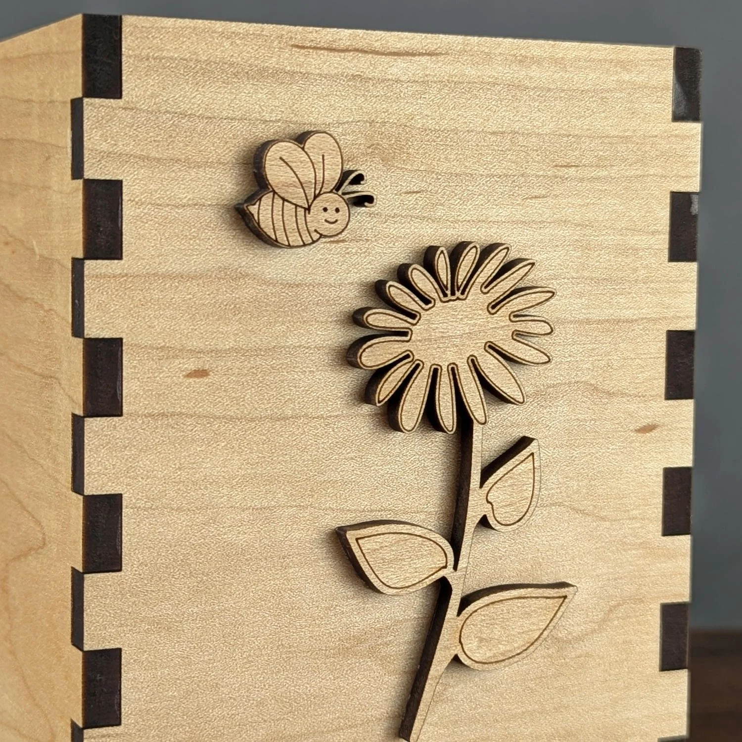 Close-up of maple vase box showing detailed laser-cut flower and bee design on natural maple wood grain.