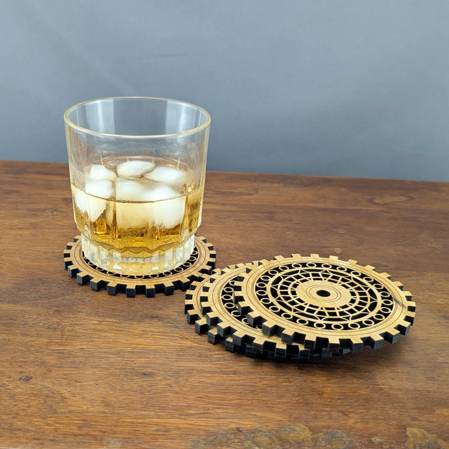 Whiskey glass on The Precisionist wooden coaster, with additional coasters stacked at an angle beside it on the table.