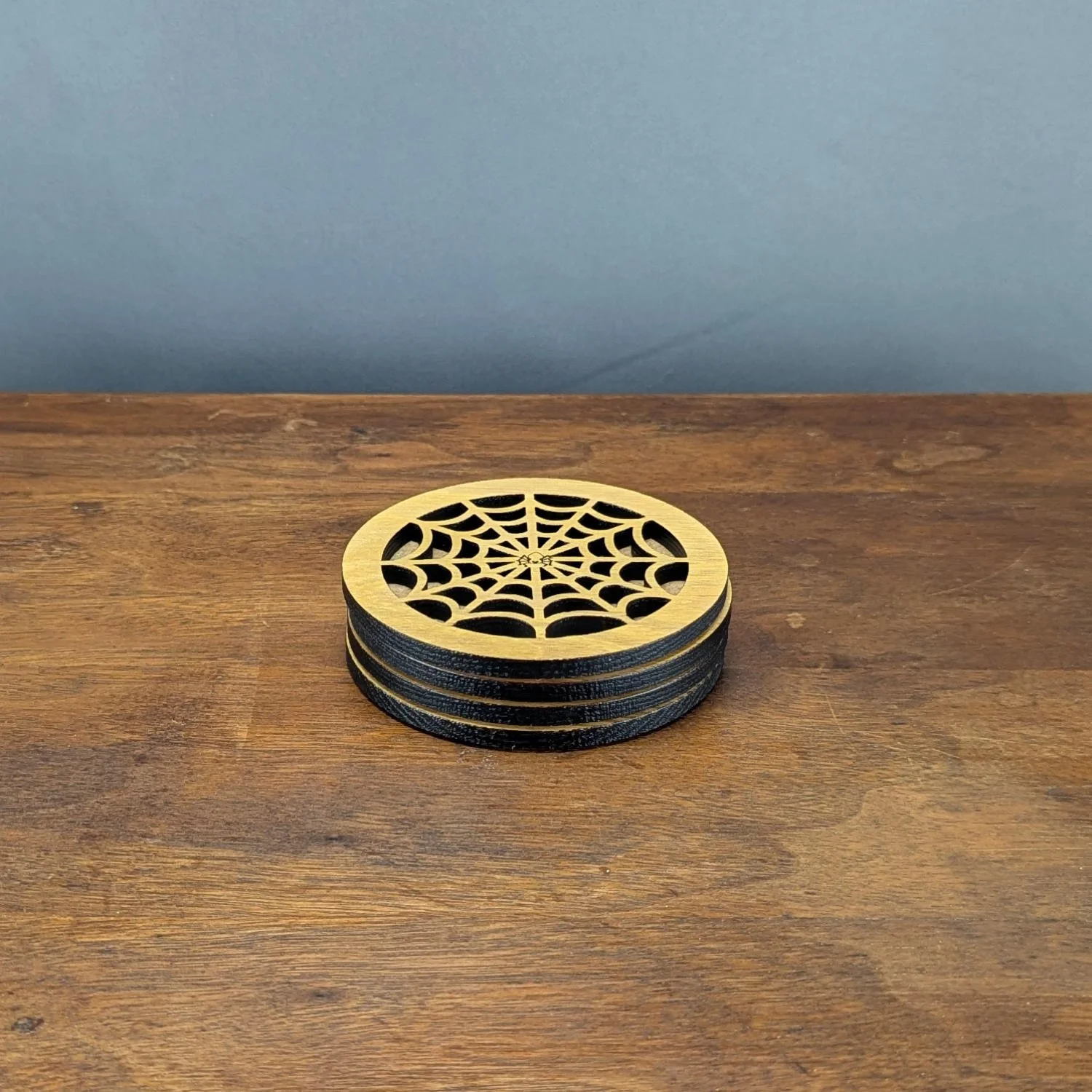 Side angle of stacked Iron Web Coasters, showing layered black edges and cut-through spiderweb design