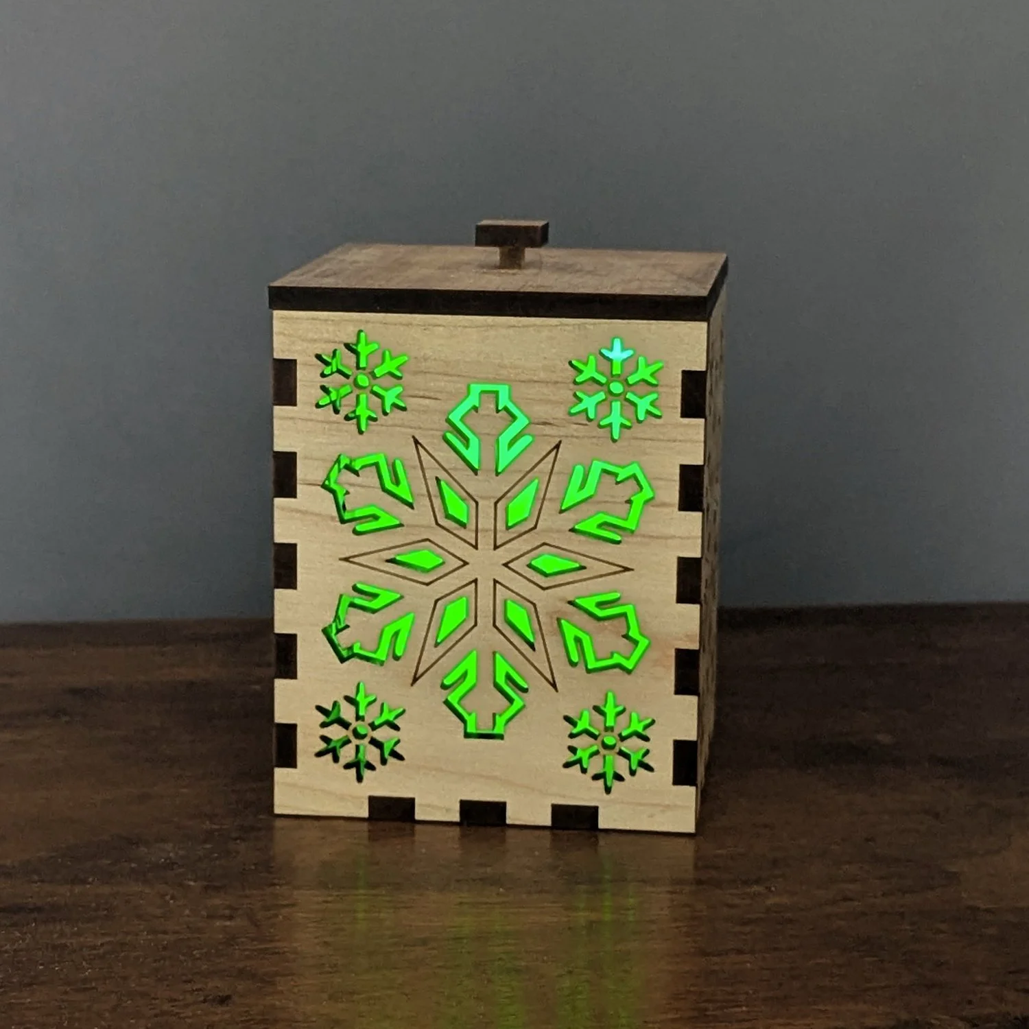 Maple Snowflake Lantern glowing green with LED candle, front snowflake pattern visible.