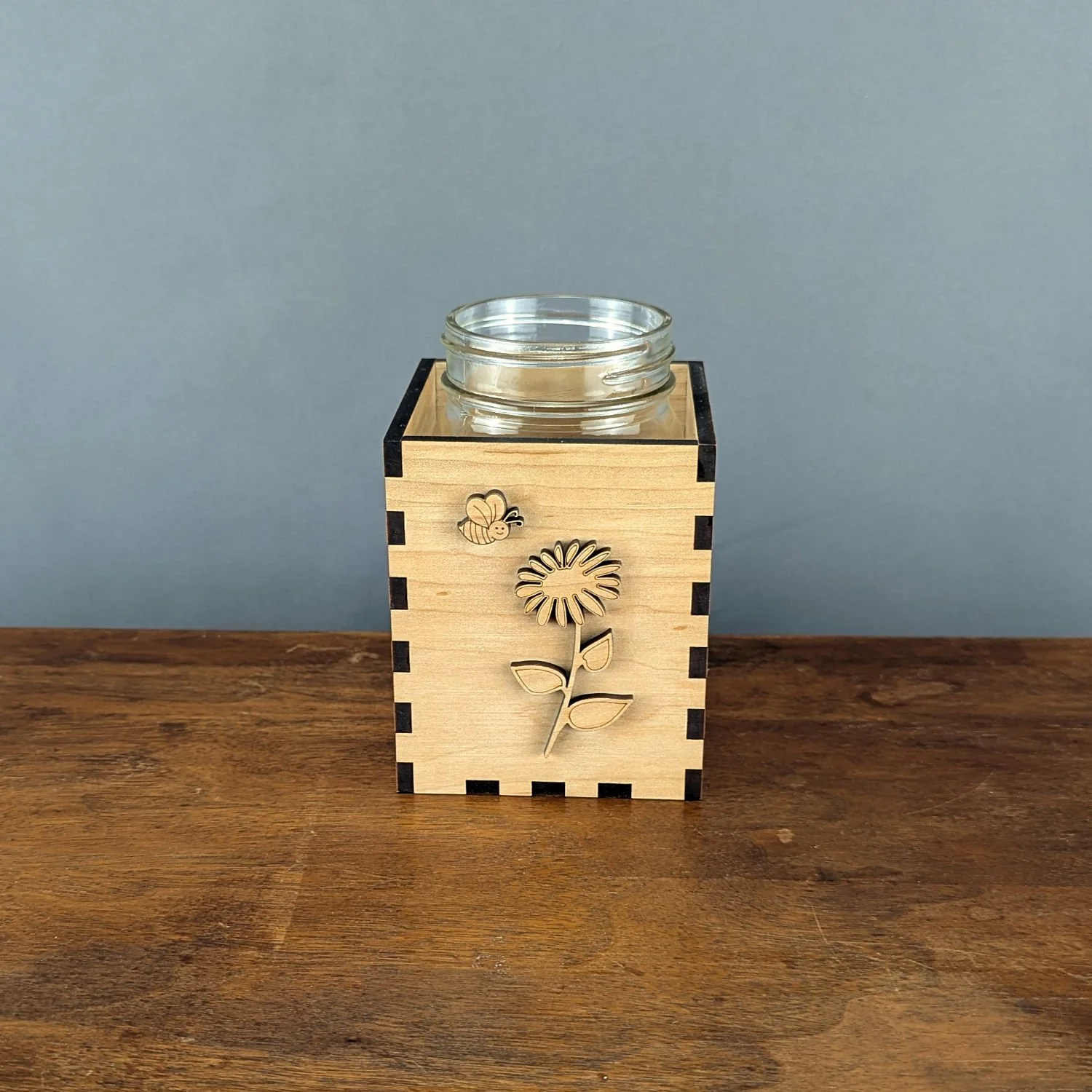 Maple wood Bloom & Buzz vase sleeve holding a mason jar insert, laser-cut bee and flower on front panel.