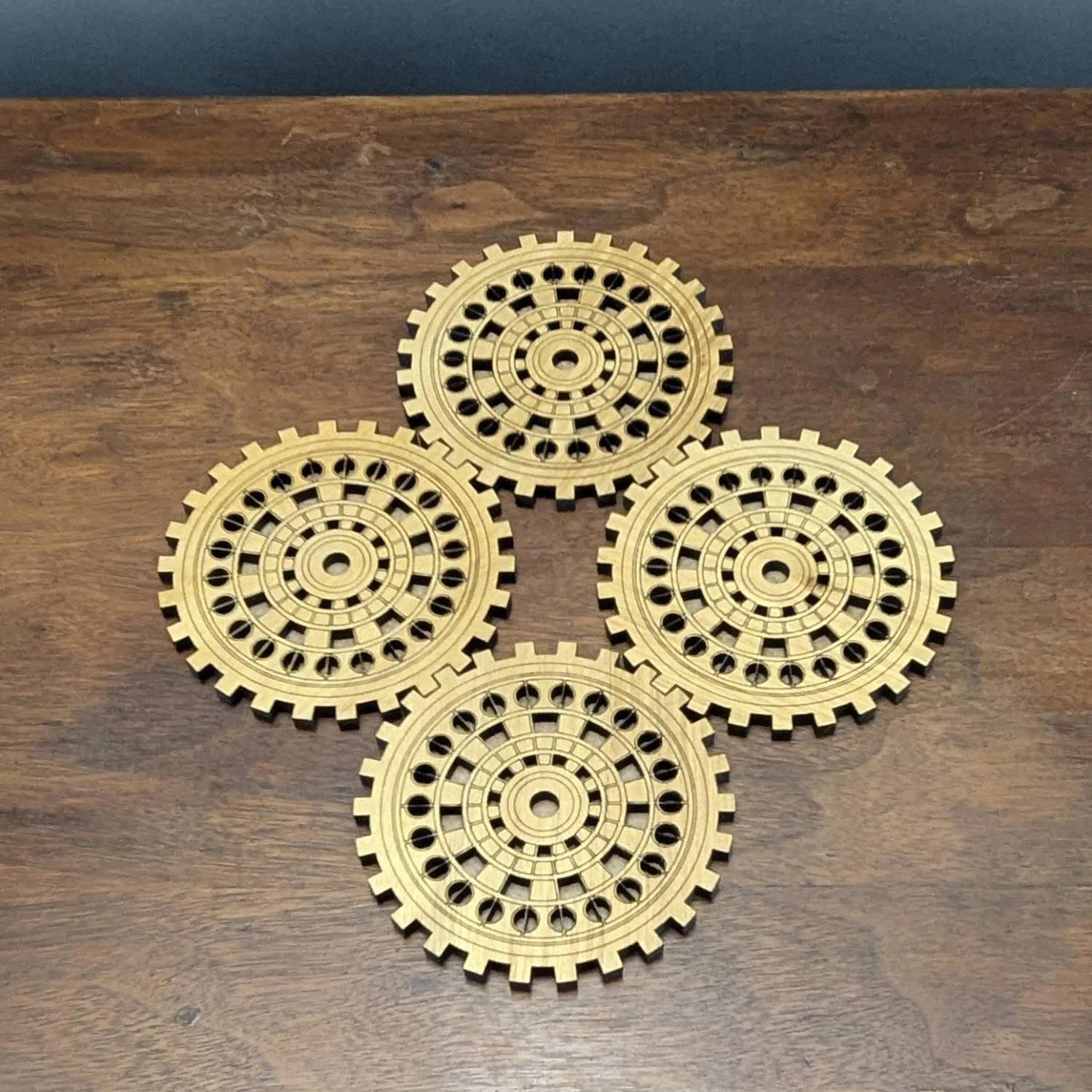 Set of four engraved wooden gear coasters arranged in a diamond formation on a wooden table.
