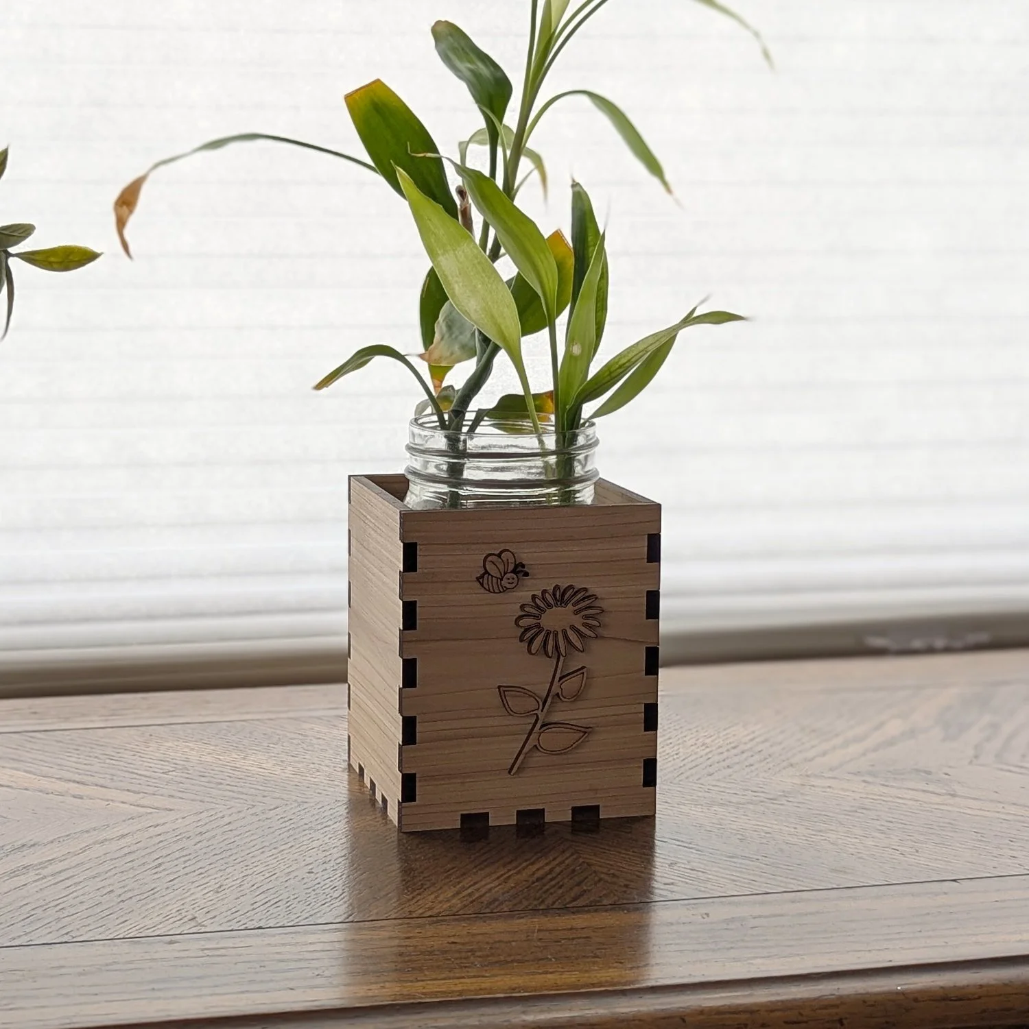 Wooden flower vase box on a table by a window, holding a plant in a mason jar.