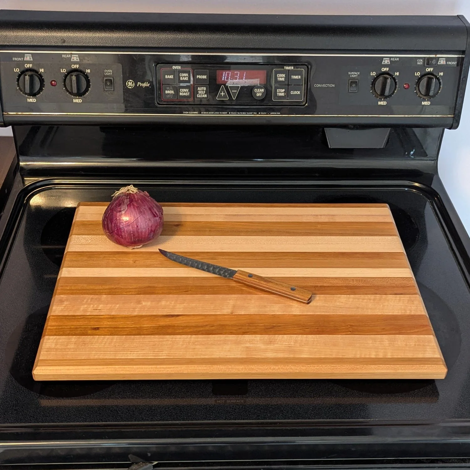 Maple and cherry cutting board on stovetop with onion and knife