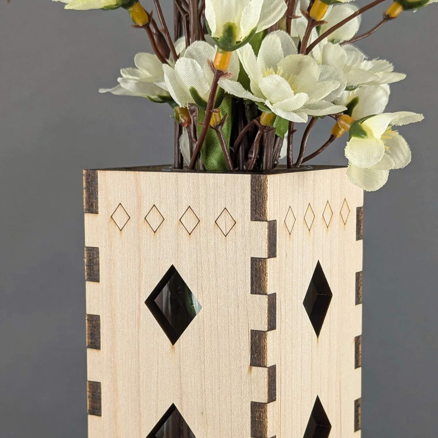 Close-up of maple vase sleeve showing diamond cutout details, finger joints, and decorative top engraving with flowers inside.