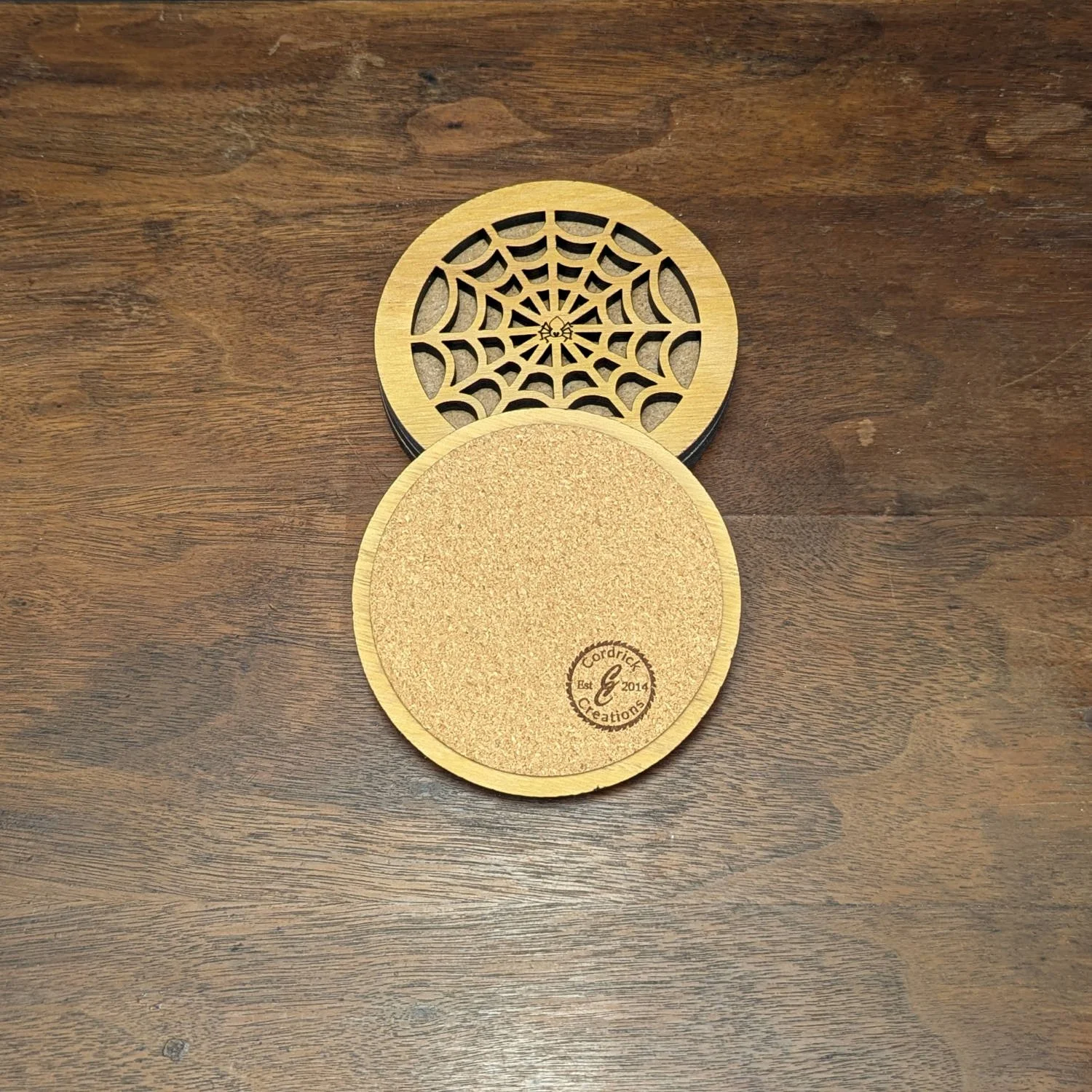 Back of Iron Web Coaster showing natural cork bottom with Cordrick Creations branding stamp, next to spiderweb cutout design