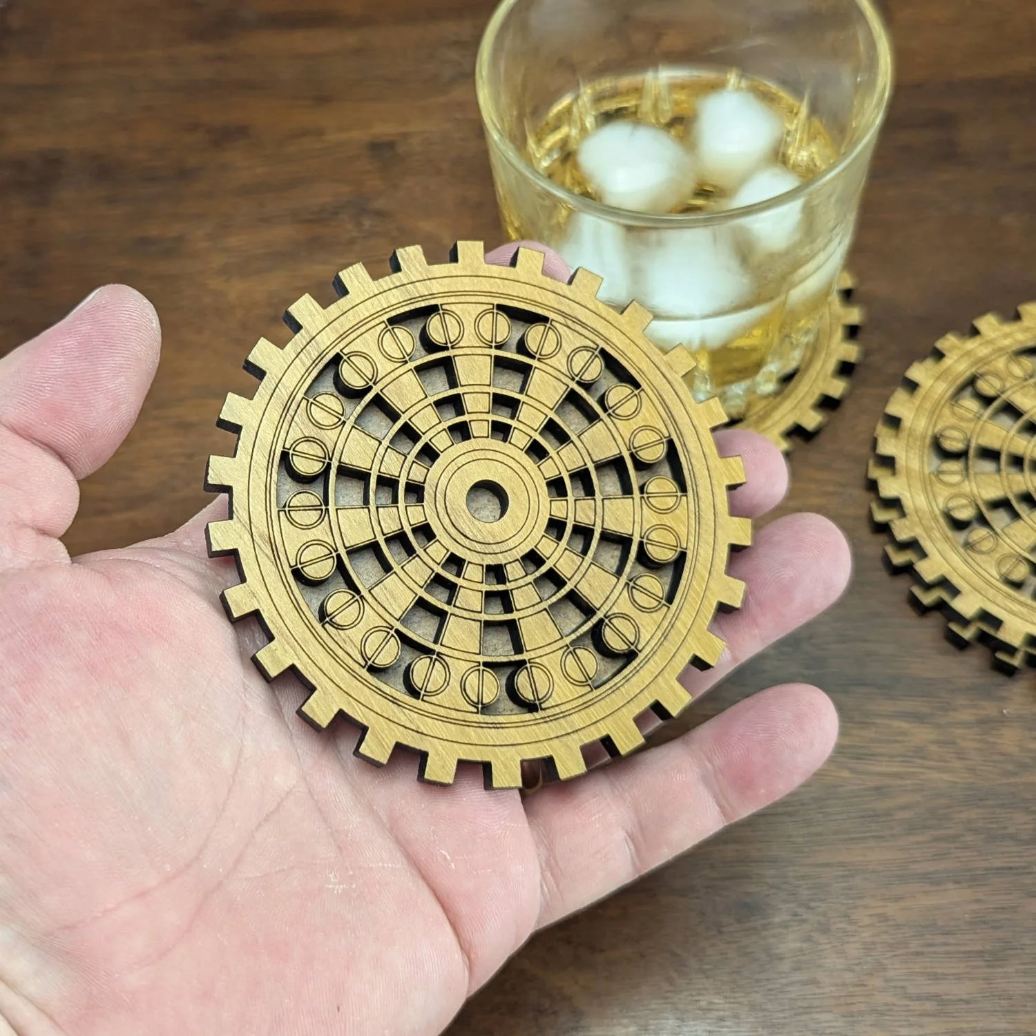 Wooden gear coaster held in hand to show size and engraved mechanical pattern.