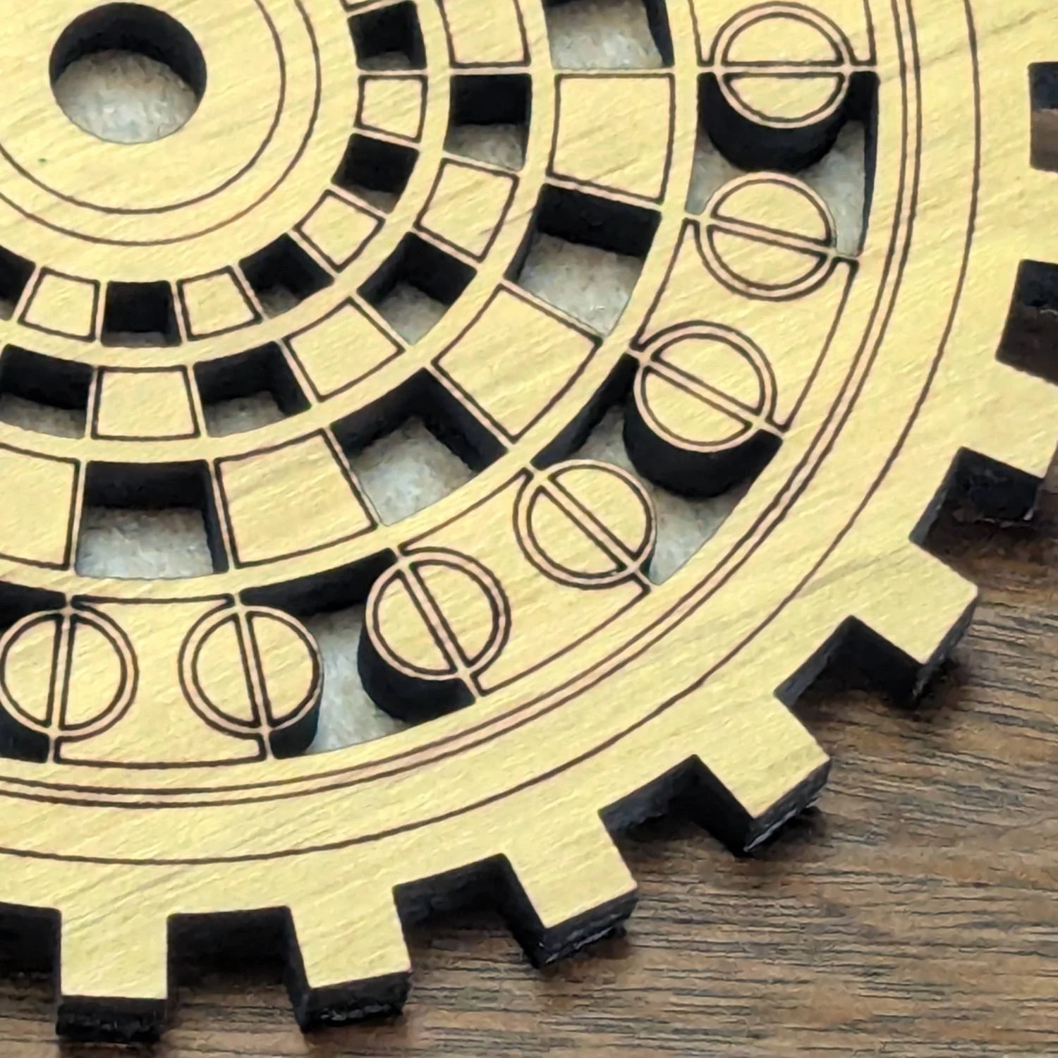 Close-up of The Operator wooden gearwork coaster showing detailed engraved dial pattern and cut edges.
