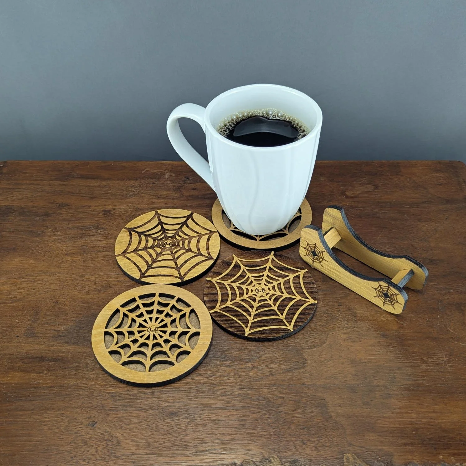 Coffee mug resting on a spiderweb wooden coaster, with additional coasters and holder displayed on a wooden table.