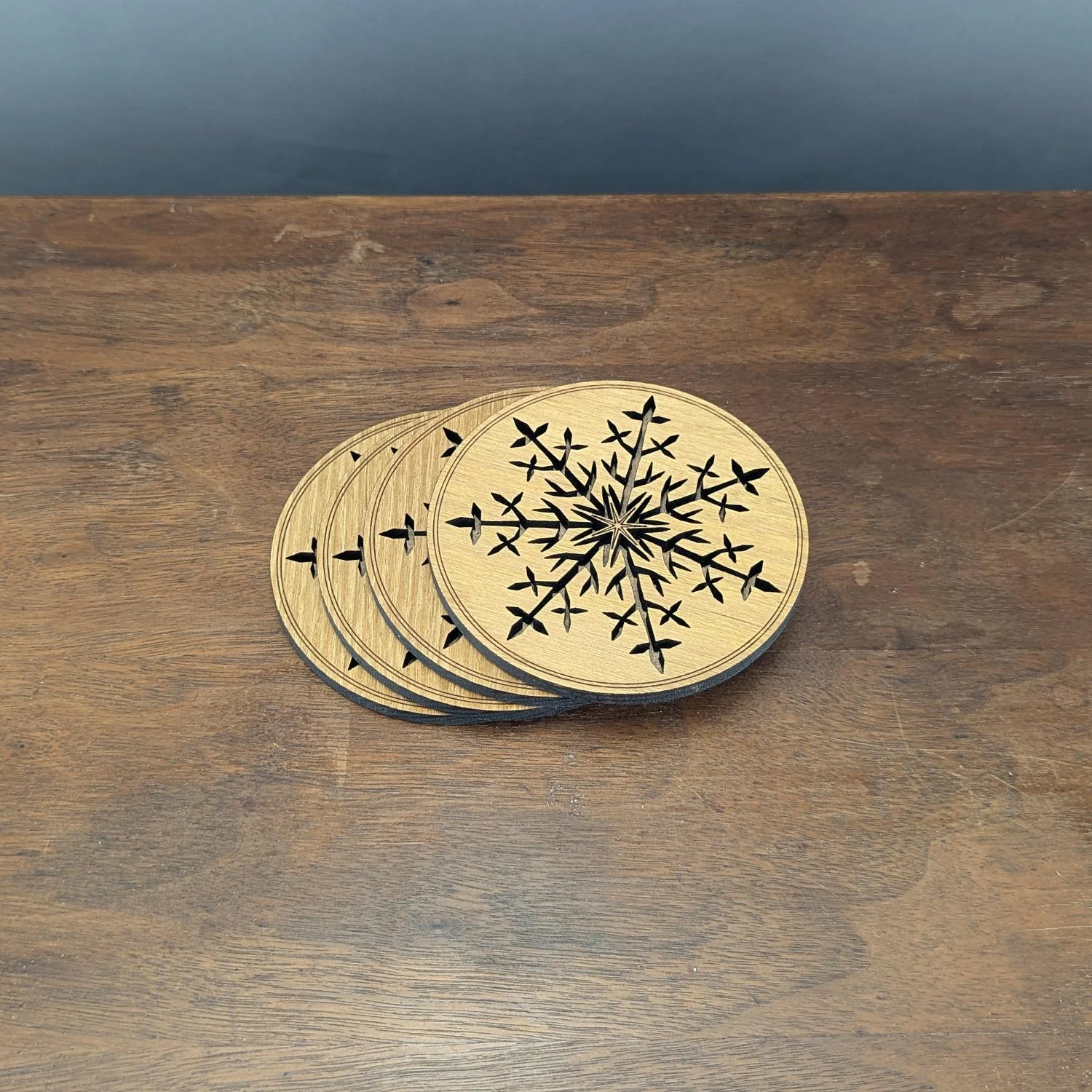 Set of four Black Locust wooden snowflake coasters displayed in a staggered stack, showing the laser-cut winter snowflake design.
