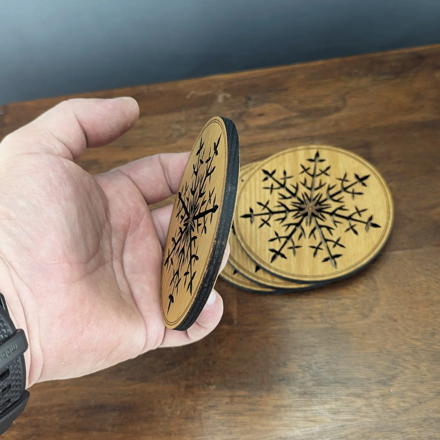 Hand holding a Black Locust snowflake coaster to show thickness and laser-cut craftsmanship.