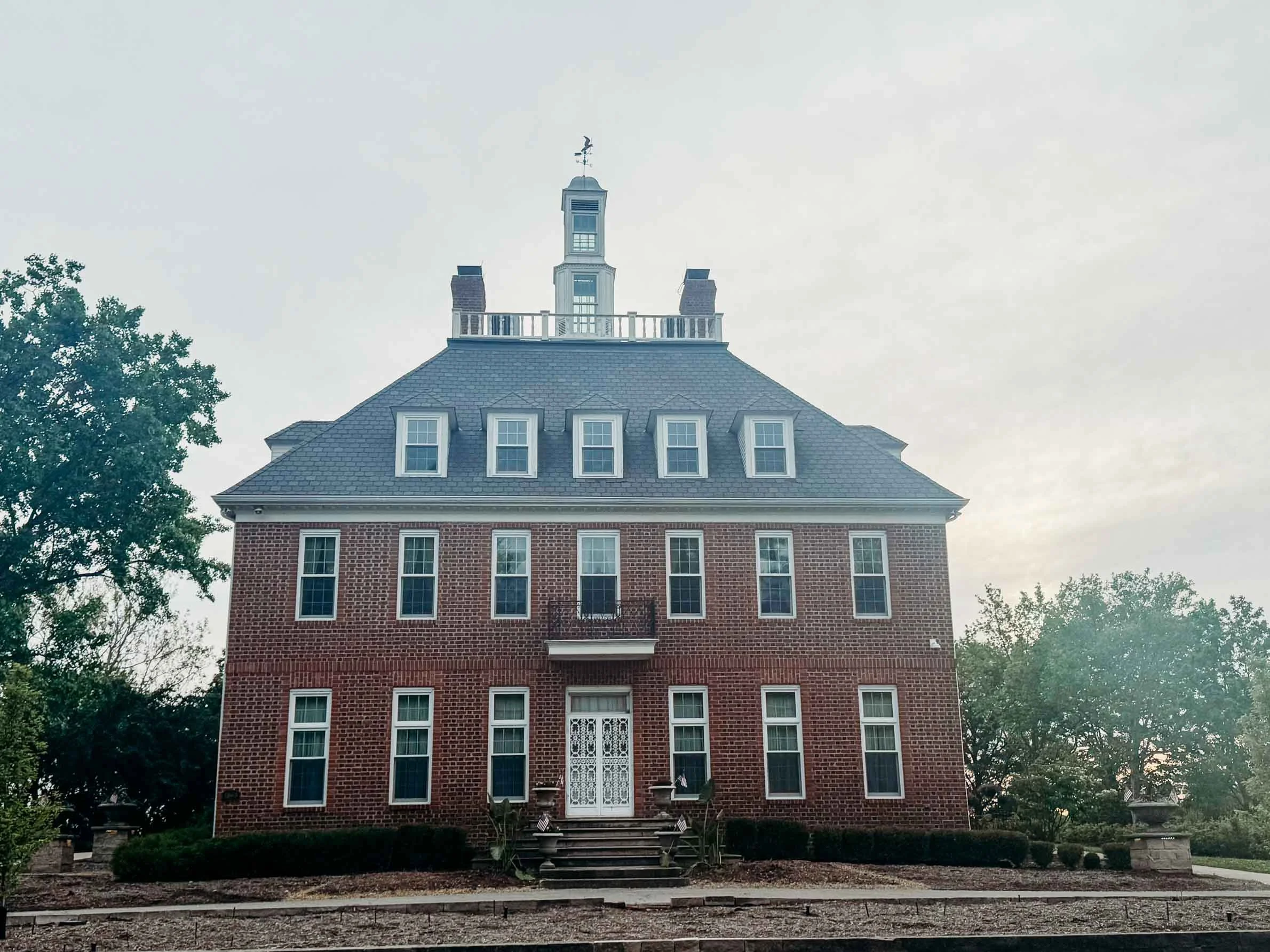 Coxhall Mansion at Coxhall Gardens in Carmel, Indiana with brick exterior, white doors, and surrounding trees.