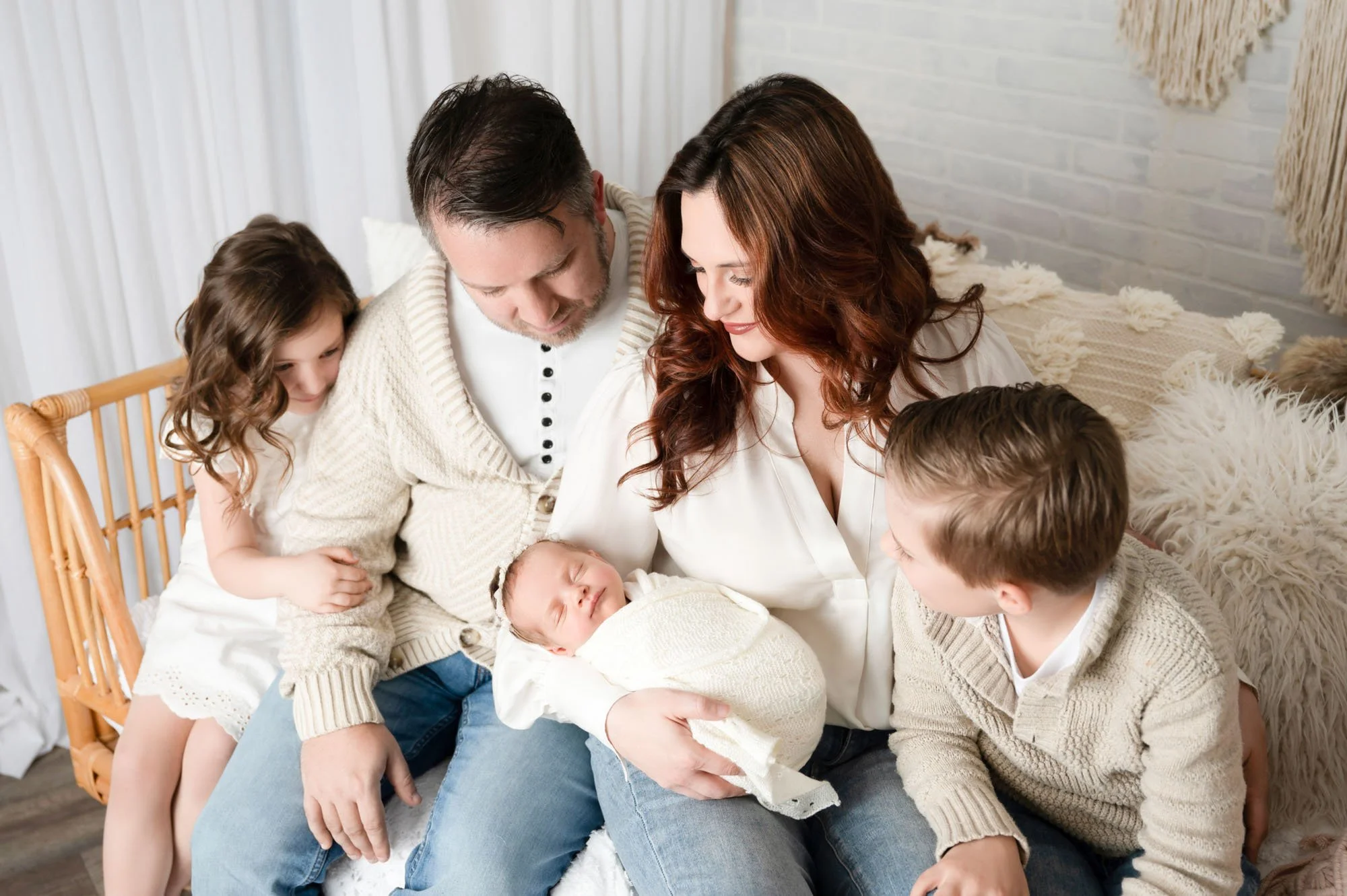 family of five sitting together looking down at newborn sibling