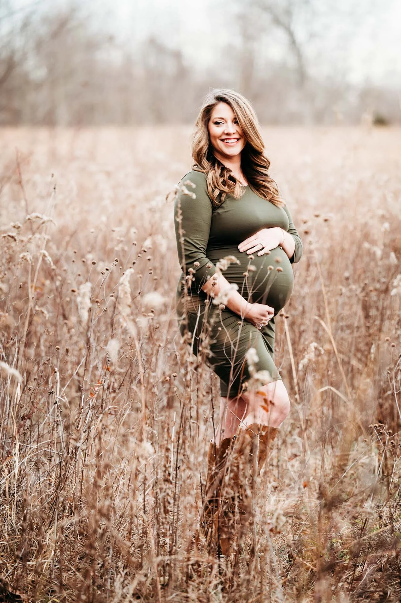 Close-up of a pregnant woman in a green dress holding her belly in a field during an outdoor maternity session in Indianapolis