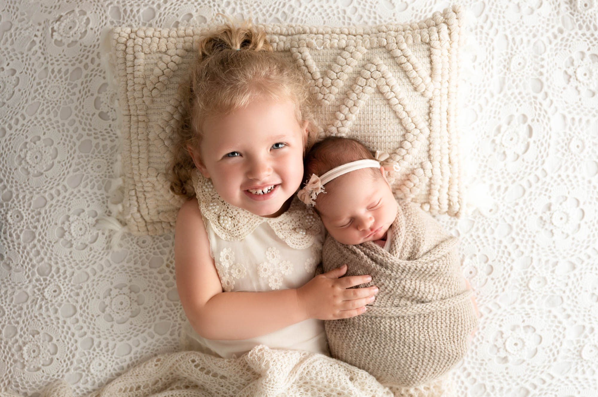 big sister laying next to newborn baby girl