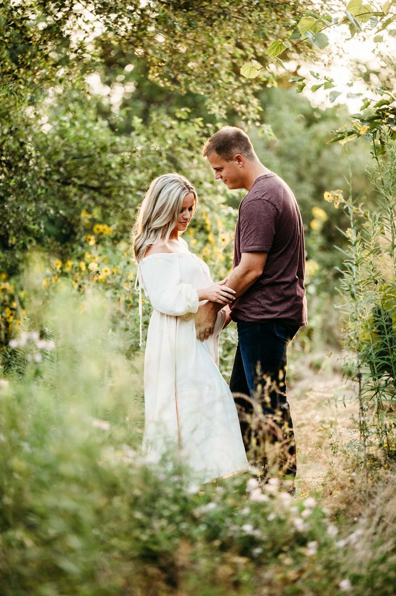 Maternity couple standing together in a wooded wildflower area at Ritchey Woods Nature Preserve in Fishers, Indiana.
