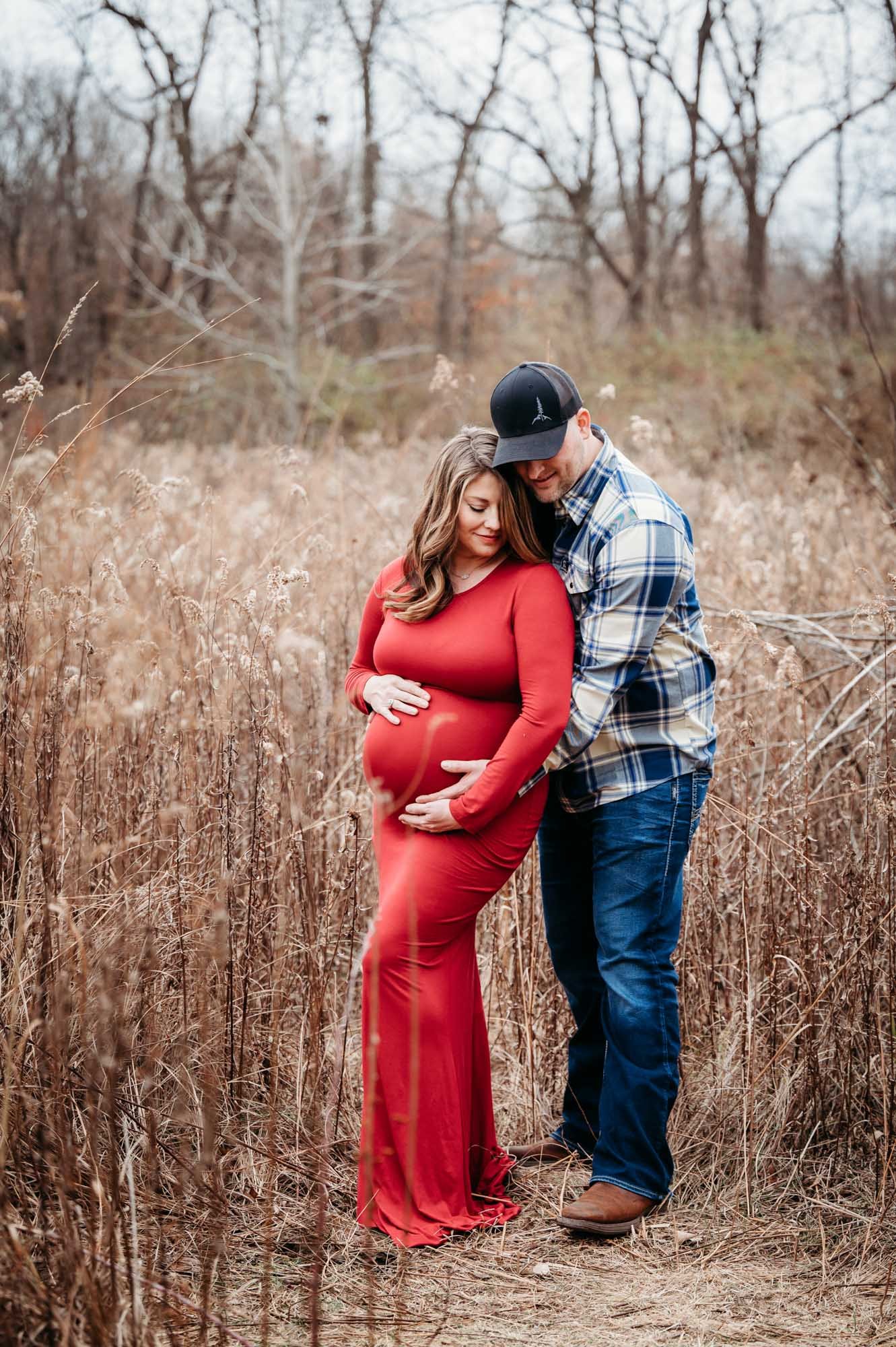 expecting couple hugging in natural field setting during Westfield, Indiana maternity photoshoot