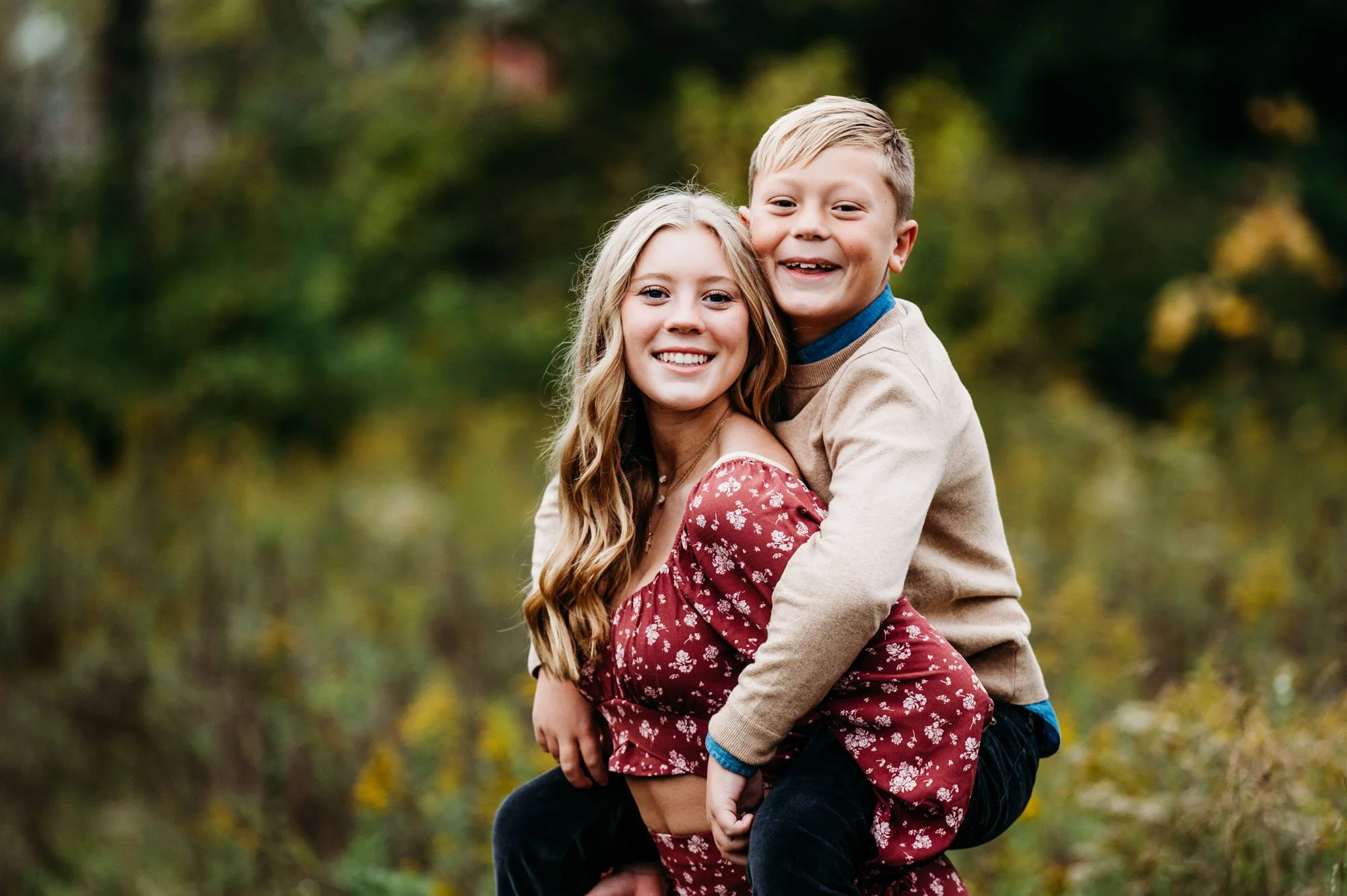 brother and sister piggyback ride in fall foliage during Carmel, Indiana family photoshoot