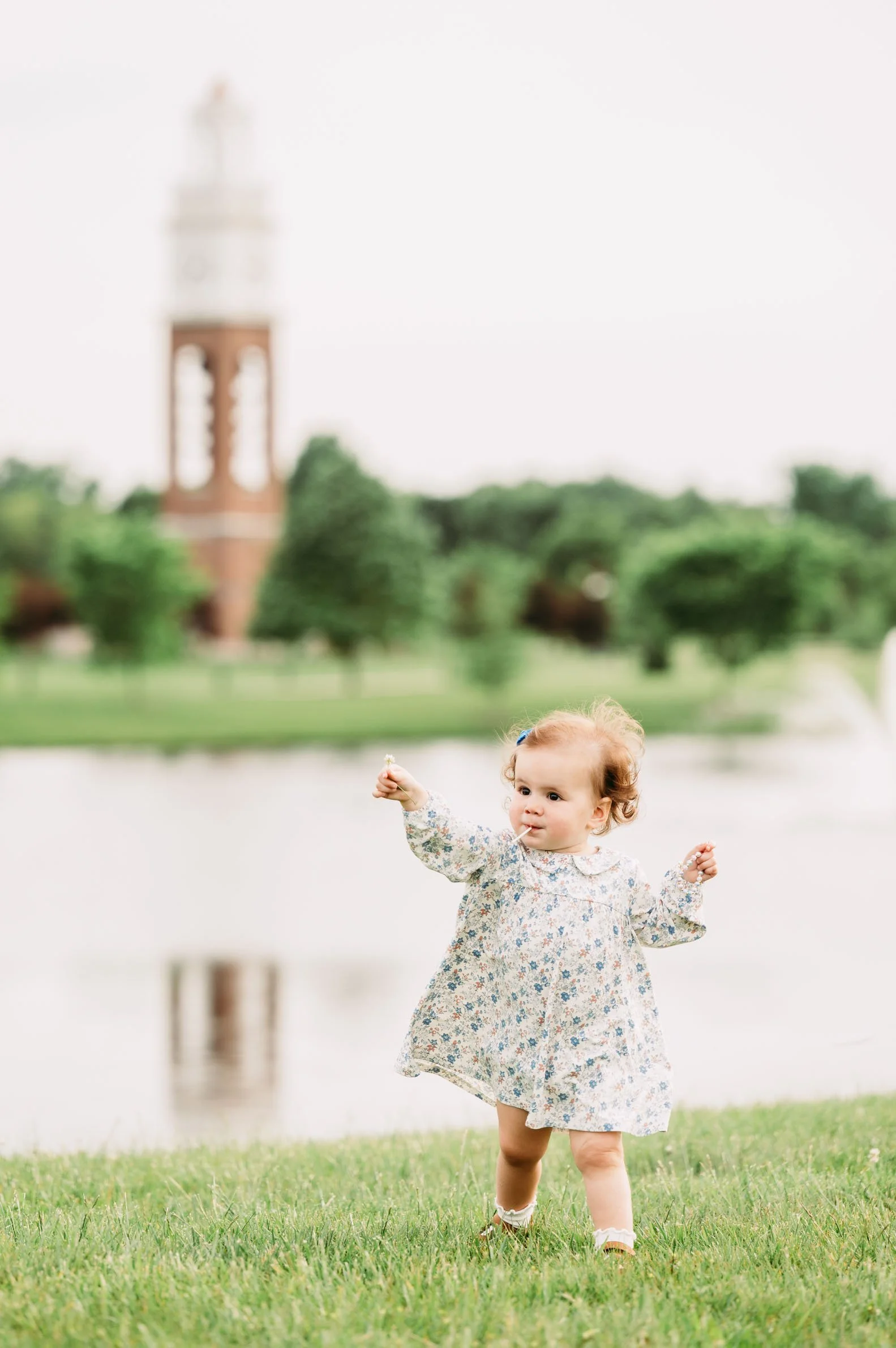 toddler playing on lawn with Coxhall Gardens clock tower in the background in Carmel, Indiana.
