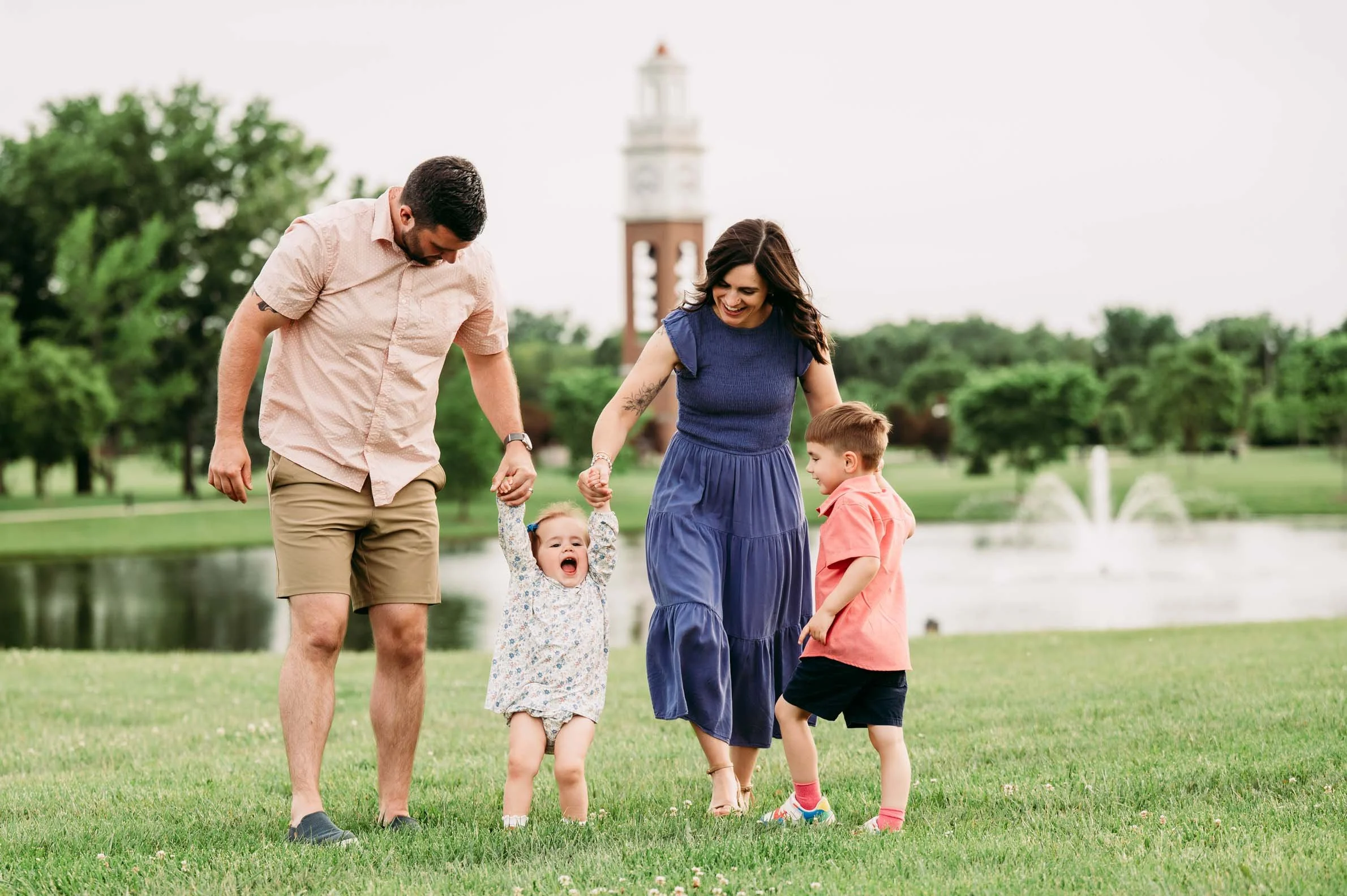 Family walking together on the lawn with the Coxhall Gardens clock tower in the background in Carmel, Indiana.