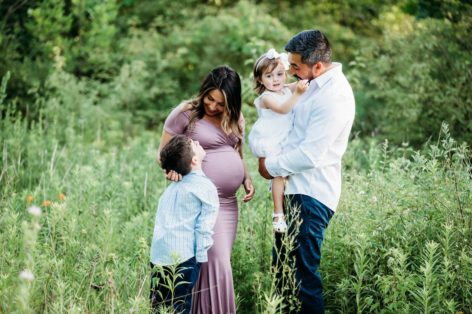 family of four having fun in tall grass during their family maternity photoshoot in Carmel, IN