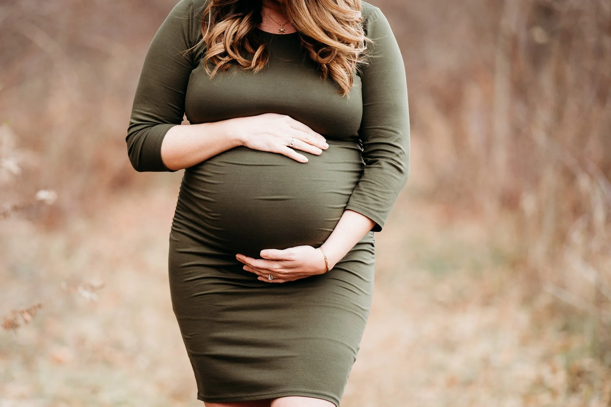 pregnant mom hugging her baby bump in a dark olive dress at her Westfield, Indiana maternity photoshoot