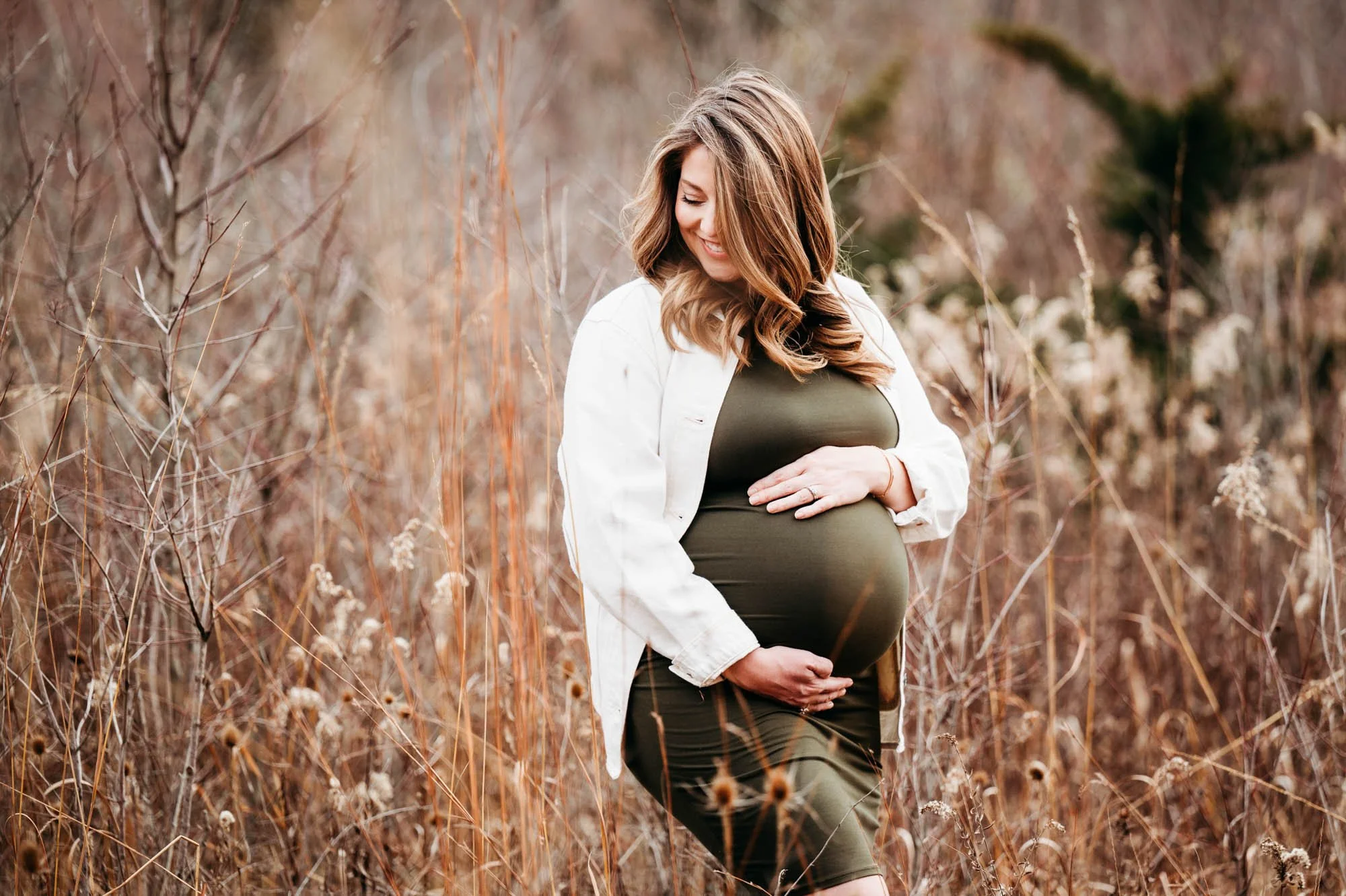 pregnant mom in a field hands on belly looking off in distance at Westfield, Indiana maternity photo shoot
