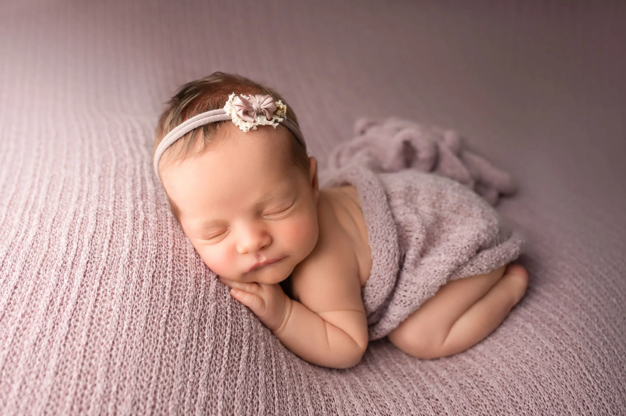 Sleeping newborn curled up on soft lavender knit fabric during Indianapolis newborn session