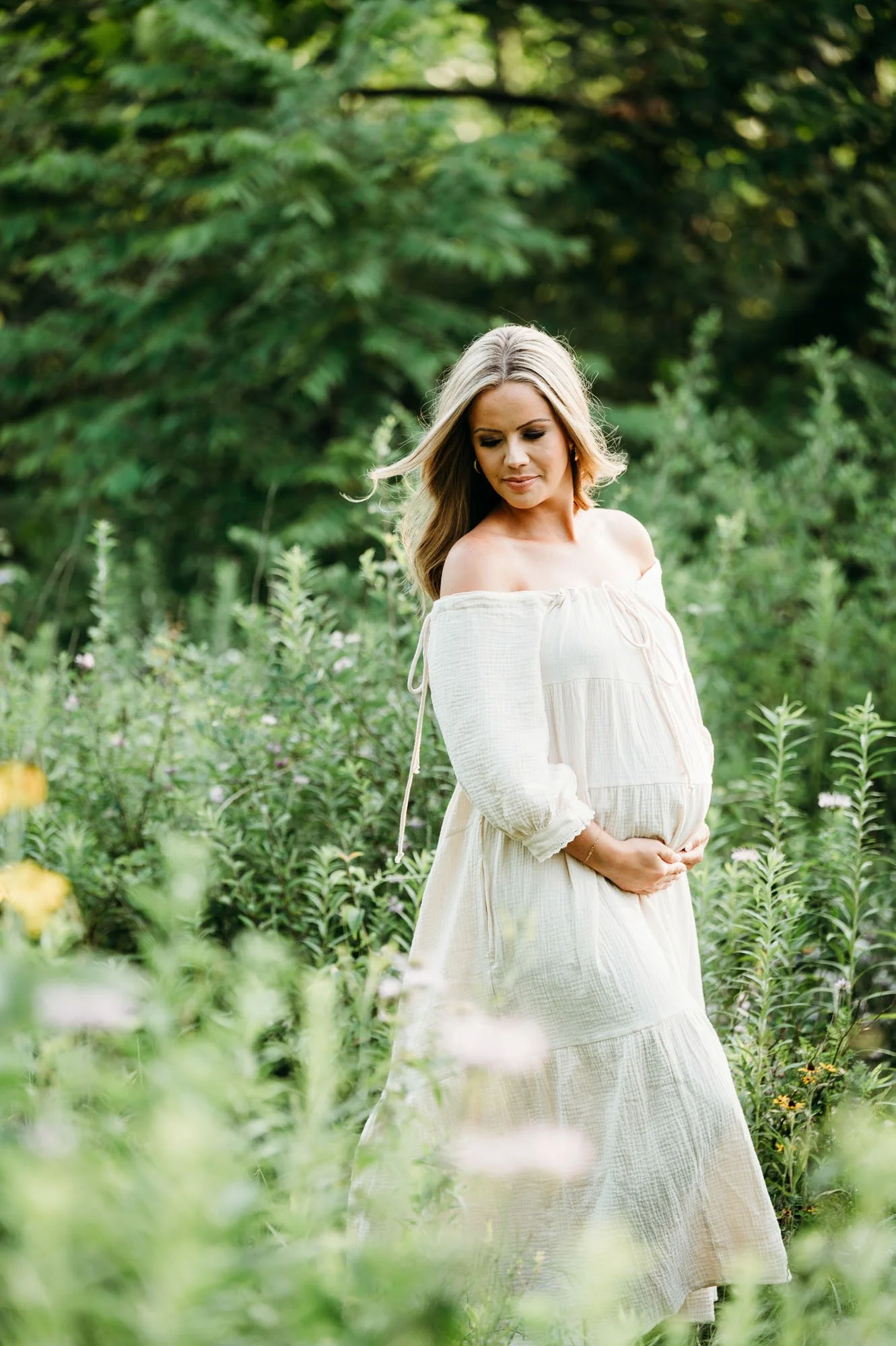 Pregnant mom in a white dress standing among greenery and wildflowers at Ritchey Woods Nature Preserve in Fishers, Indiana.
