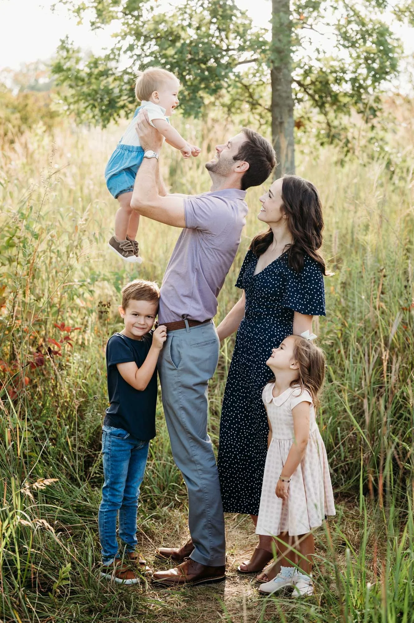 Father lifting his baby while the rest of the family looks on during an outdoor Noblesville, Indiana family photoshoot