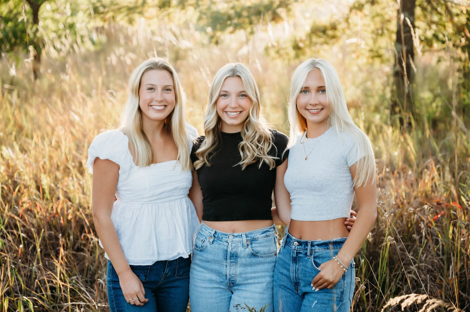 Three sisters posing together outdoors in a grassy field during a family photography session during Westfield, Indiana family photos