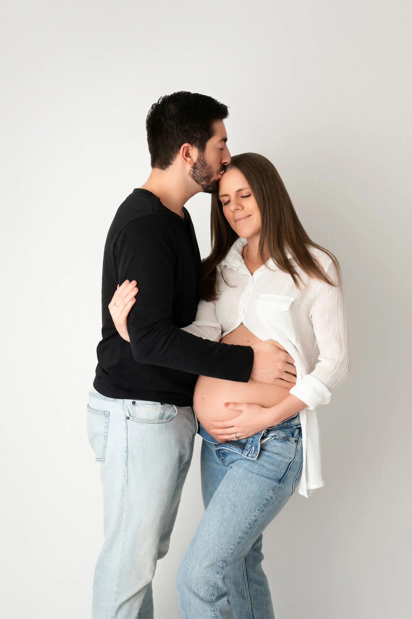 couple expecting baby standing together with Dad kissing mom in Noblesville, Indiana maternity photoshoot