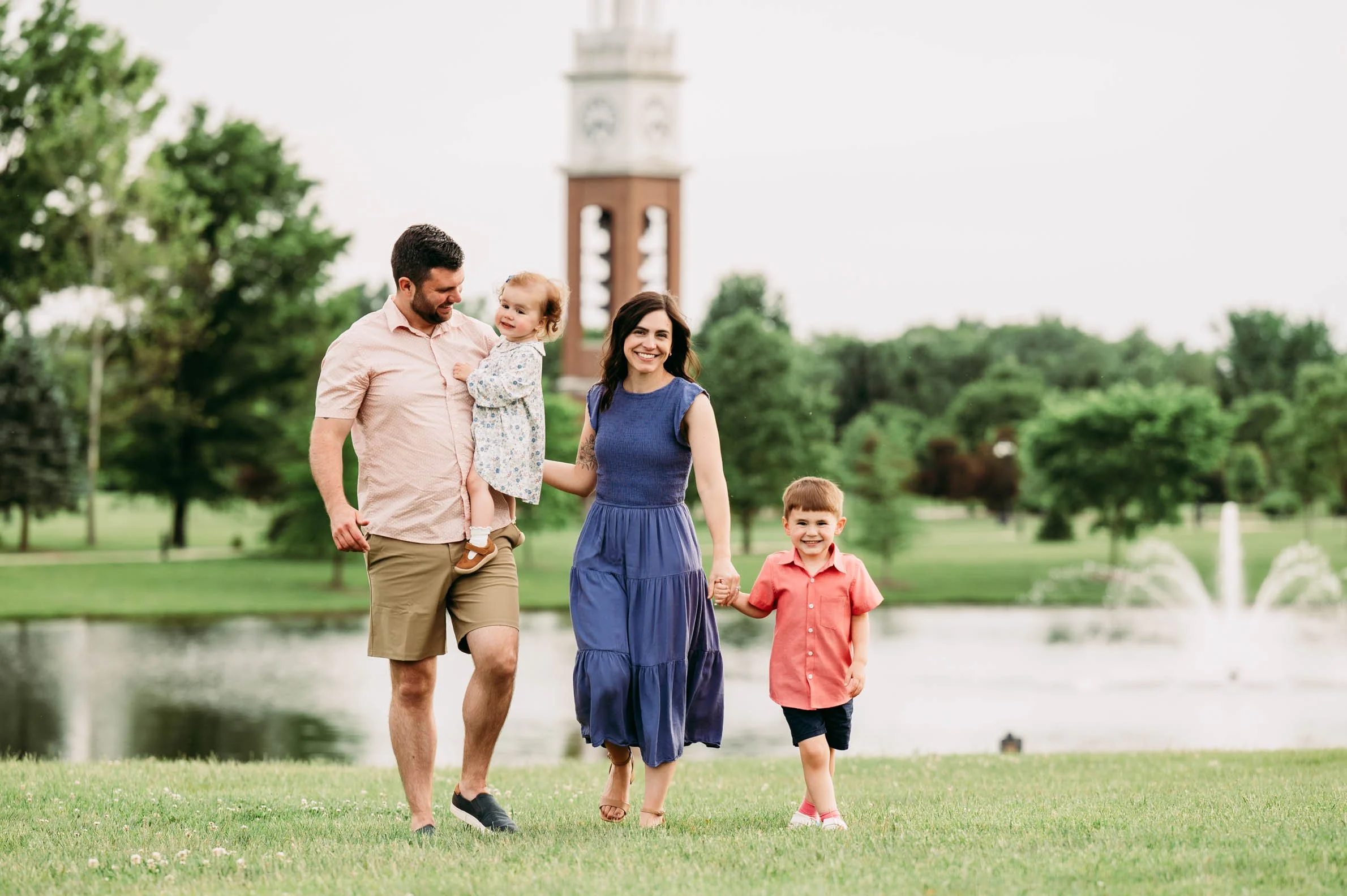 Family walking together by the pond with the Coxhall Gardens clock tower in the background in Carmel, Indiana.