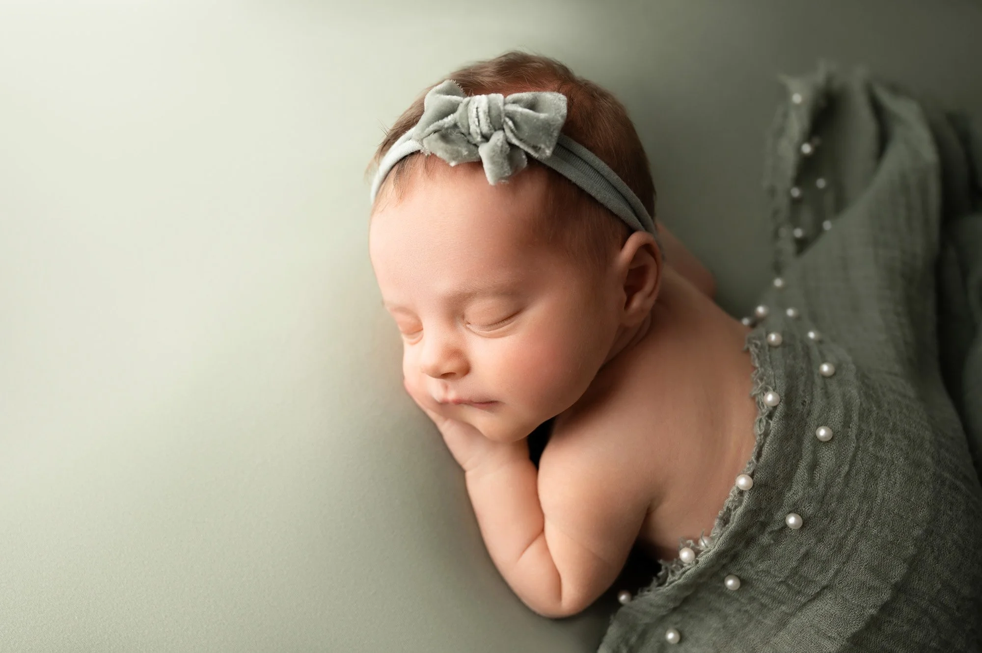newborn baby girl sleeping on sage fabric with velvet bow headband during Indianapolis newborn session