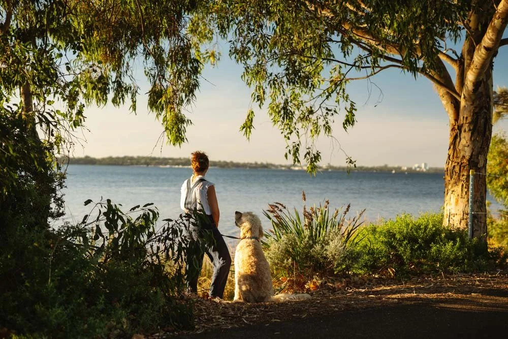Emily Hirshman-Smith, Perth Anxiety & Depression Counsellor and Psychotherapist, with her dog looking out through the lush green trees across the lake.